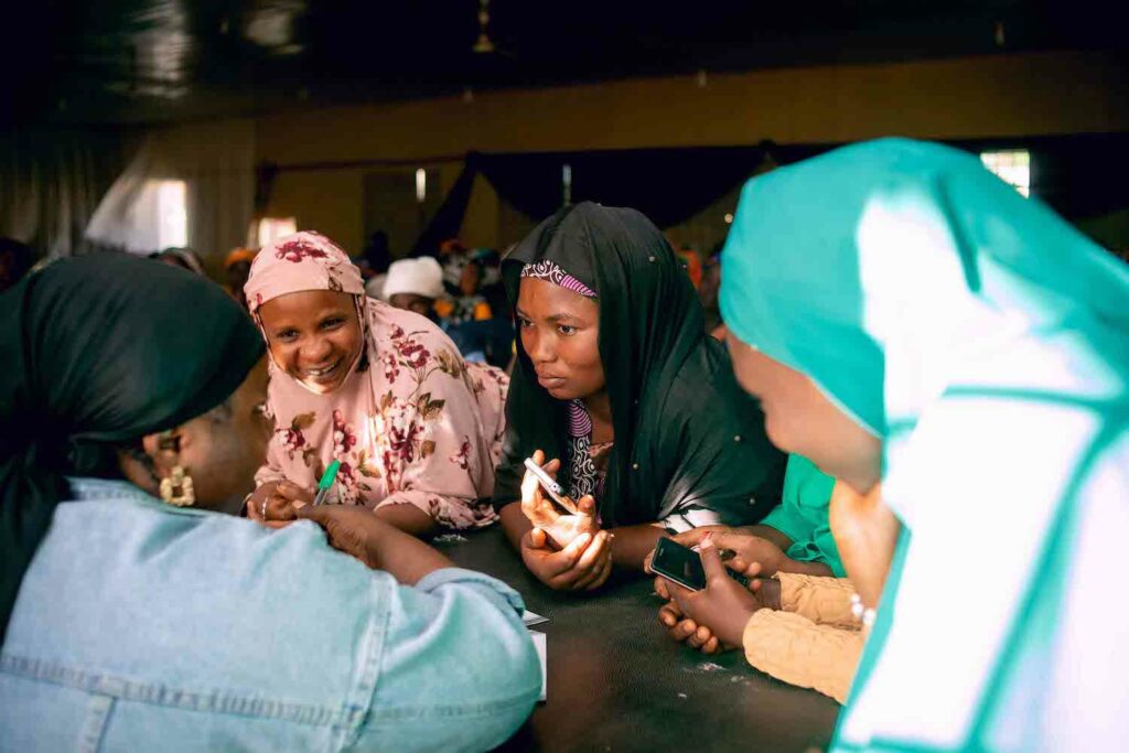 A group of women from Women's Cooperative Societies with headscarves sitting around a table, working towards economic empowerment in partnership with GPF Nigeria.