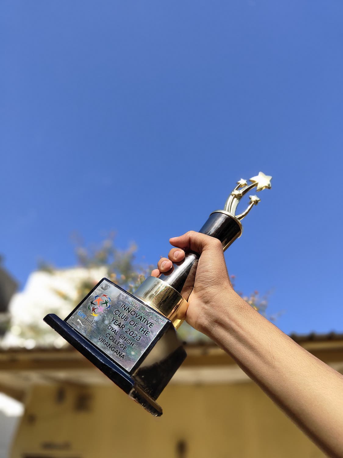 A person holding up a trophy against a clear blue sky, celebrating victory in youth peace clubs' January 2024 event.