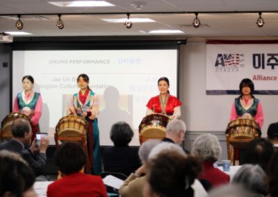 Three women in traditional Korean attire perform a drumming presentation for an audience at a forum commemorating the March 1 Movement.
