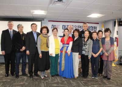 Group of individuals standing together for a photo, some wearing traditional Korean attire, in a room with South Korean flags in the background to commemorate the March 1 Movement.
