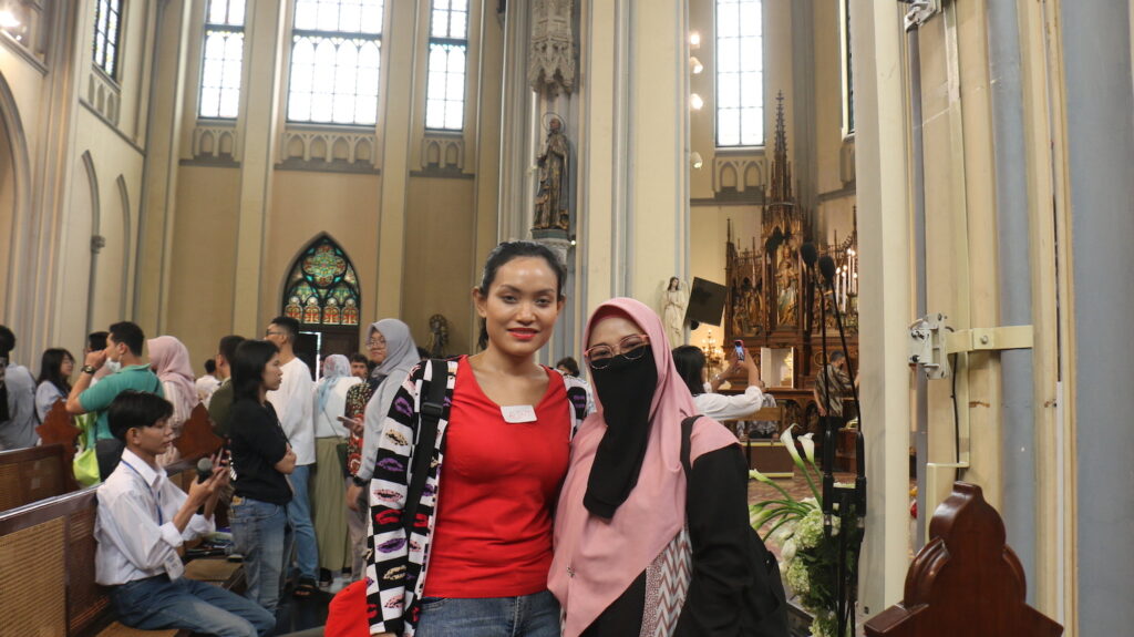 Two women posing for a photo inside the Jakarta Cathedral Church with other people in the background for the Peace Project.