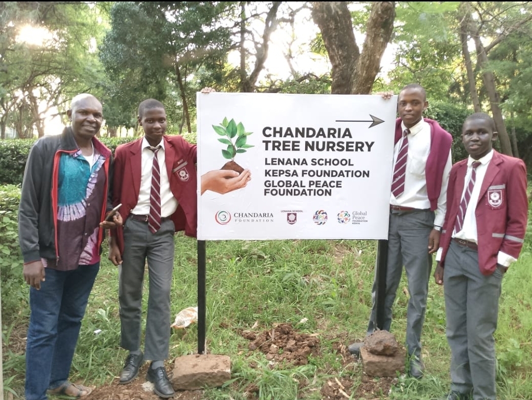 Four individuals posing with a sign for "Chandaria Tree Nursery" at Lenna School in Kenya, in collaboration with KEPSA Foundation and Global Peace Foundation, supporting sustainable development.