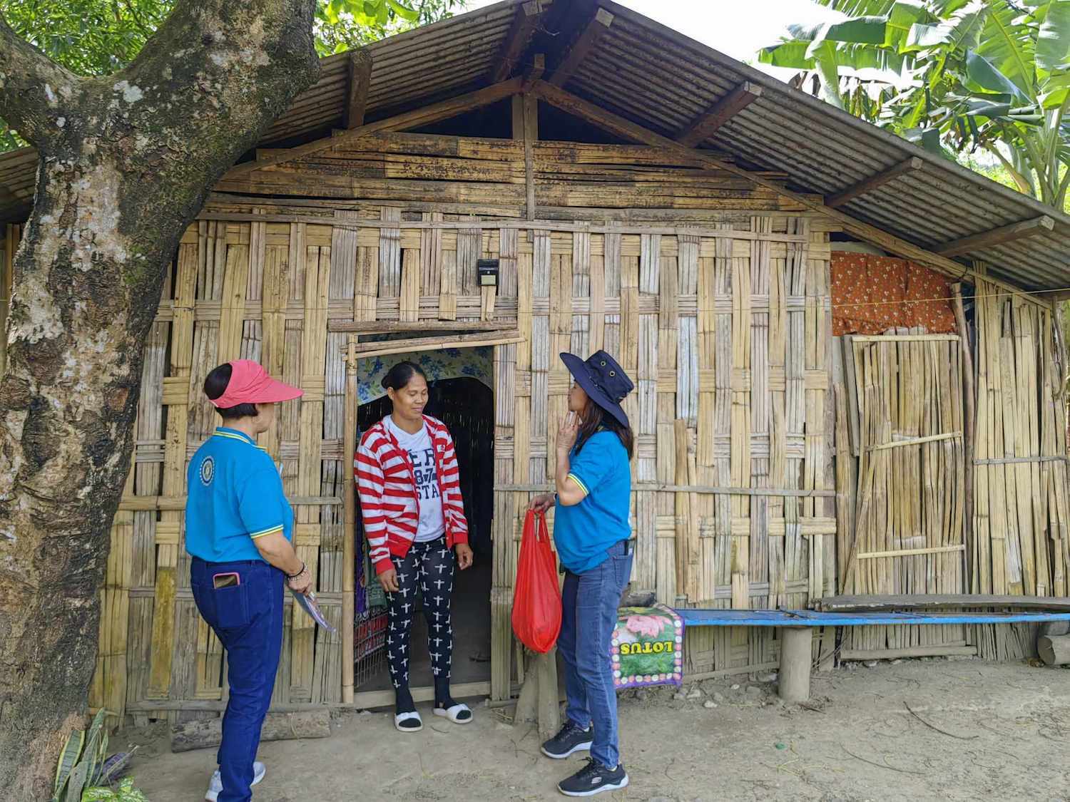 Two individuals in blue uniforms representing the Inner Wheel Club of Central Ortigas are having a conversation with a person in front of a traditional bamboo house.