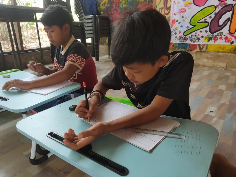 Two students focused on writing in their notebooks at a classroom table in remote villages, thanks to the initiatives by GPF Malaysia on education.