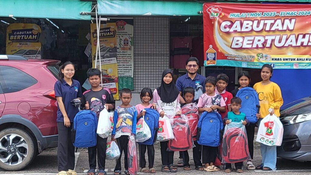 Group of adults and children from remote villages standing in front of a store, holding new backpacks provided by GPF Malaysia for education.