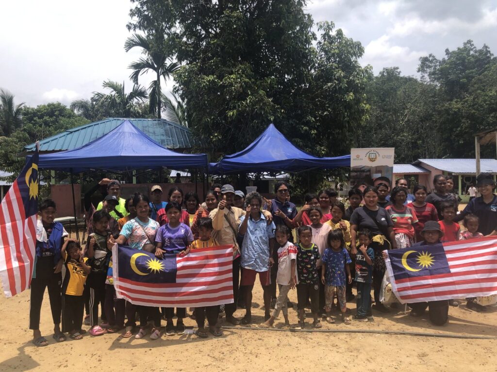 Group of people from remote villages holding Malaysian flags outdoors at a GPF Malaysia community gathering.