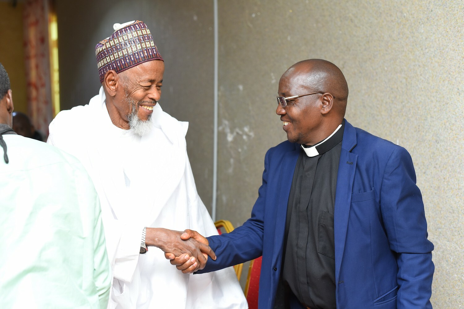 Two men in traditional and religious attire commemorating Interfaith Harmony Week 2024 in Nigeria, shaking hands and exchanging smiles.
