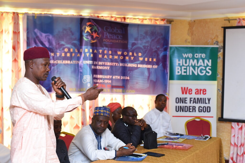 A man speaks at a podium during Nigeria Interfaith Harmony Week 2024, emphasizing unity and peace, with attendees listening in the background.