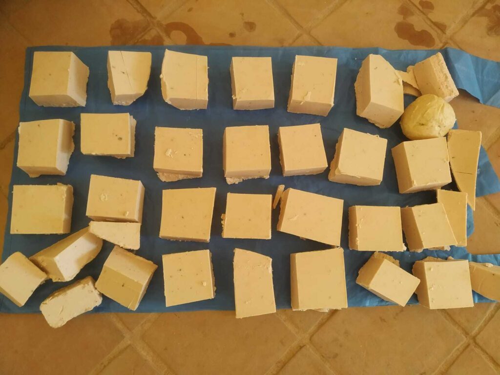 Multiple blocks of environmentally-friendly homemade cheese on a blue cloth, with some pieces broken open to reveal the texture.