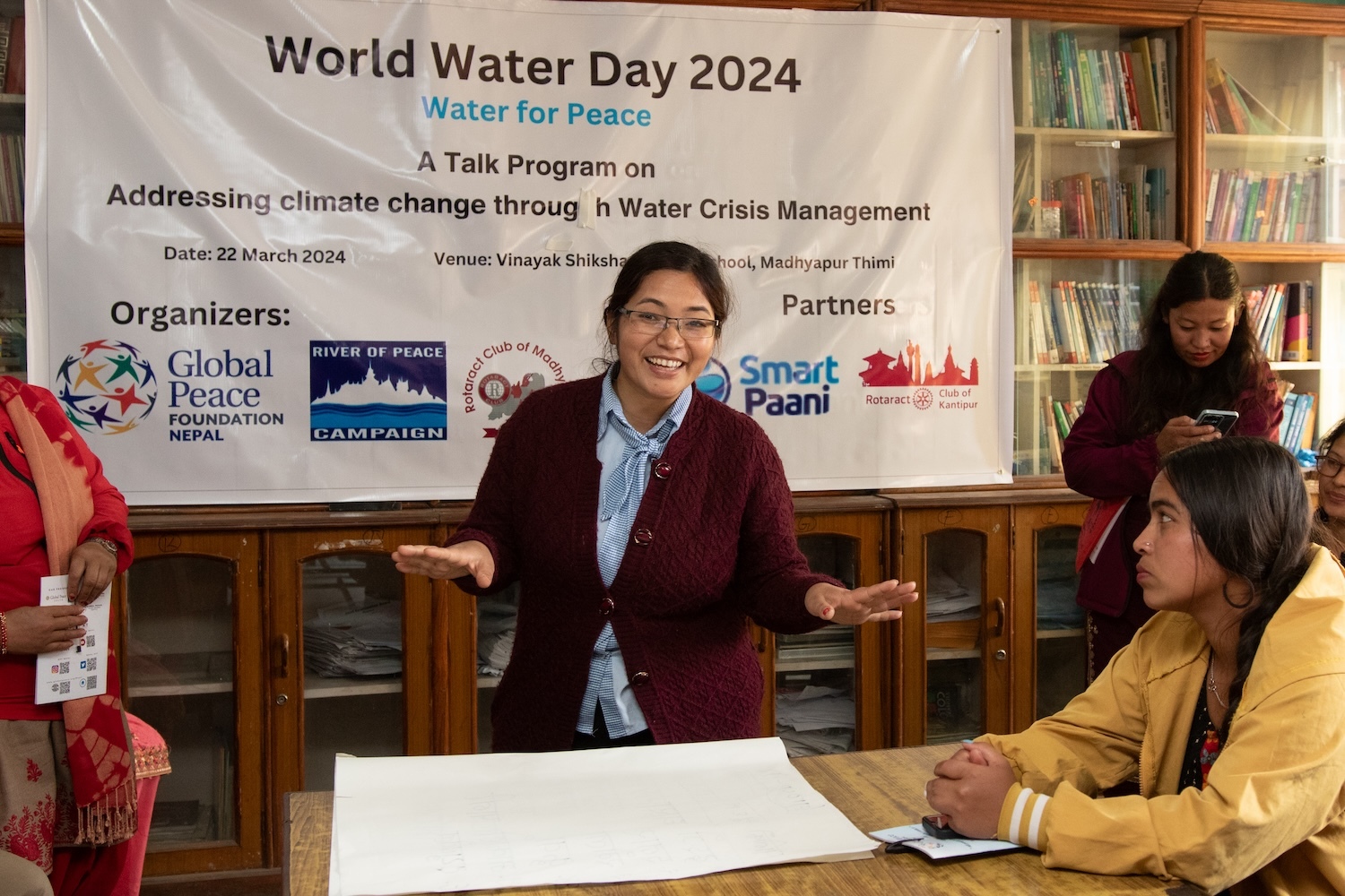 Woman at a World Water Day 2024 smiling at the camera, with attendees and informational banners in the background.