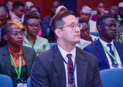 A diverse group of people, dressed in business attire, attentively listening at a conference or meeting on environmental issues. Most individuals have lanyards around their necks with "GPLC Africa 2024" prominently displayed, indicating the specific track they are following.