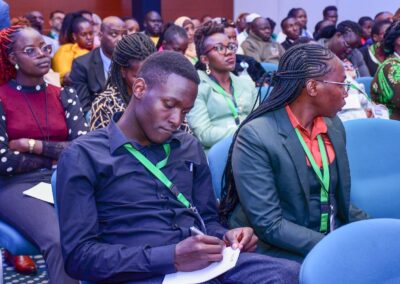 A group of people seated in rows, attentively listening to a presentation at GPLC Africa 2024. A man in the foreground is taking notes while a woman beside him looks ahead. Many attendees are wearing lanyards, marking their participation in the Environmental Track.