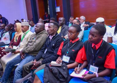 A diverse group of people, including students in uniform and individuals in traditional attire, sit attentively in rows at the GPLC Africa 2024 event, taking notes and listening to insights from the Environmental Track.