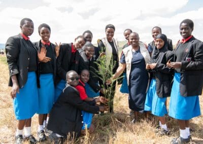 A group of students in school uniforms gathered around a newly planted tree with a few adults in a field, participating in the Kenya National Tree Growing event as part of GPLC Africa 2024.