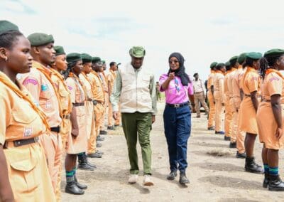 A man and a woman walk between two lines of uniformed individuals standing at attention outdoors during the Kenya National Tree Growing Campaign.