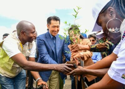 A group of people, some in uniforms, collaboratively plant a young tree sapling outside on a clear day as part of the Kenya National Tree Growing Campaign.