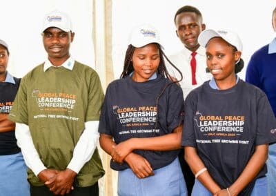 A group of young people wearing t-shirts and caps from the Global Peace Leadership Conference stand together at the Kenya National Tree Growing Event, as part of the GPLC Africa 2024 Campaign.