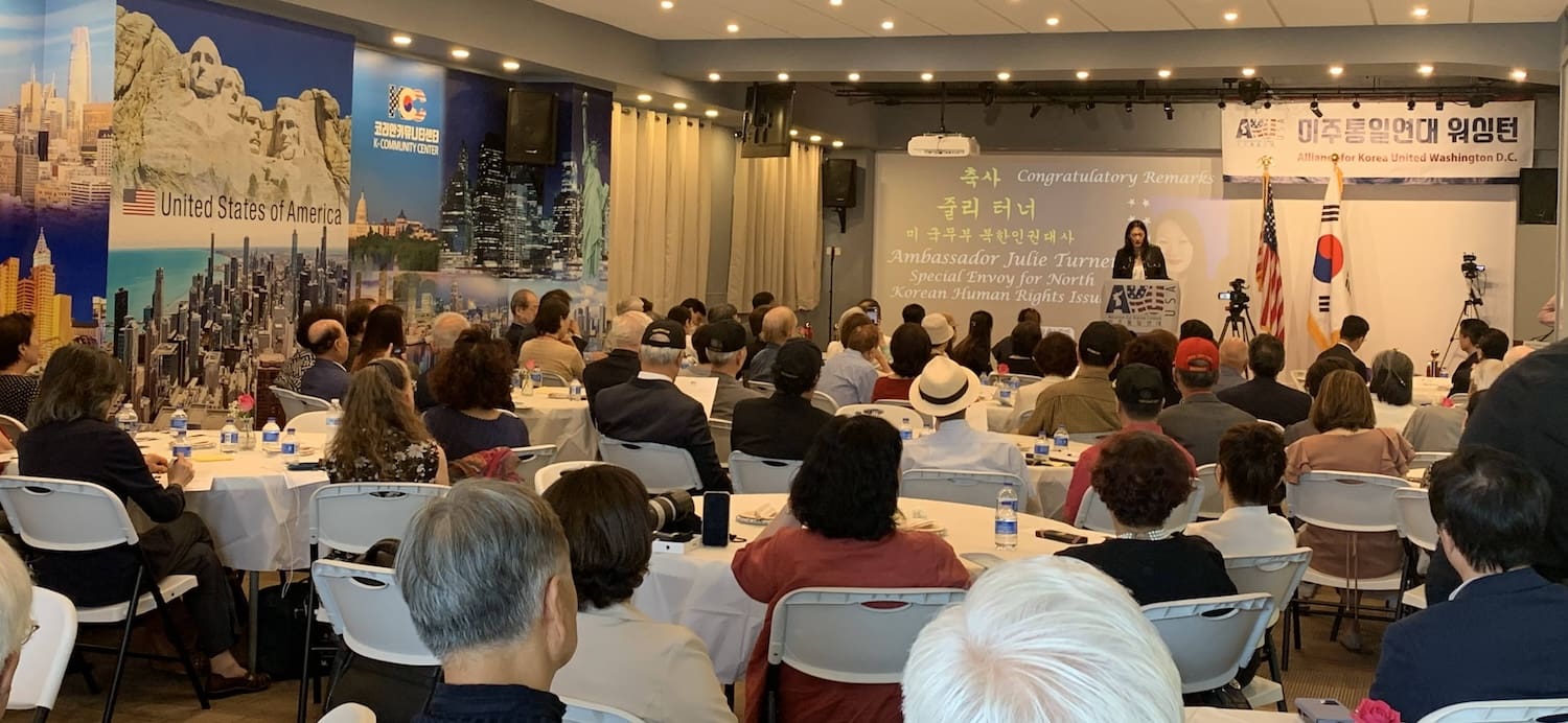 A woman speaks on stage in a conference room with