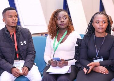 Three people with conference badges sit in a row at GPLC Africa 2024; two women and one man. The woman in the center holds a phone and notebook, clearly highlighting her involvement in the Education Track. All appear attentive.