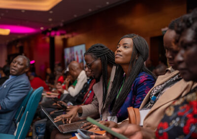 A group of people sit attentively in a conference room at the GPLC Africa 2024 plenary, with some taking notes on laptops and others looking forward. The setting appears formal and focused.