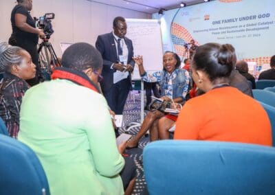 Participants engage in discussion at the "One Family Under God" conference, part of the Education Track at GPLC Africa 2024, focused on peace and sustainable development in Nairobi, Kenya. A woman gestures while others listen intently.