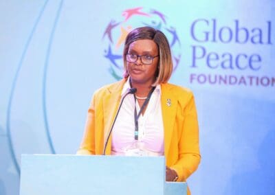 A person in a yellow blazer speaks at a podium in front of a backdrop that reads "Global Peace Foundation" during the GPLC Africa 2024 conference, emphasizing the crucial role of education in fostering global harmony.