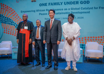 Four men stand on stage in front of a blue backdrop with the text "One Family Under God," during the GPLC Africa 2024 plenary event in Nairobi, Kenya, June 25-27. They are dressed in formal and traditional attire.