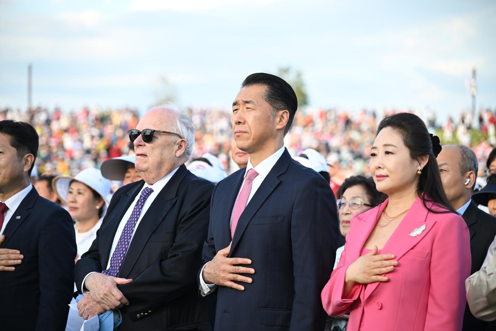 A group of people, including an elderly man and two middle-aged adults, standing with their right hands over their hearts in a powerful show of solidarity during an outdoor event.