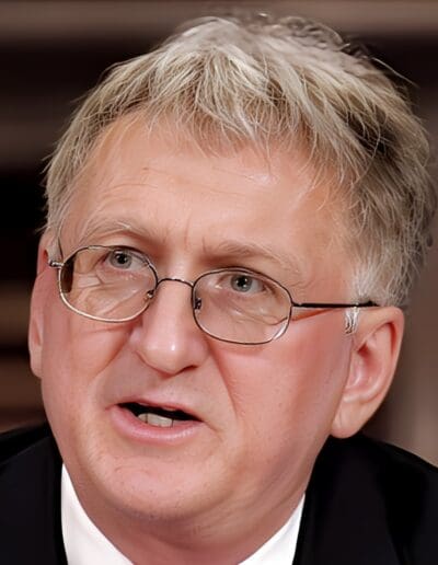 A man with gray hair, glasses, and a suit is speaking.