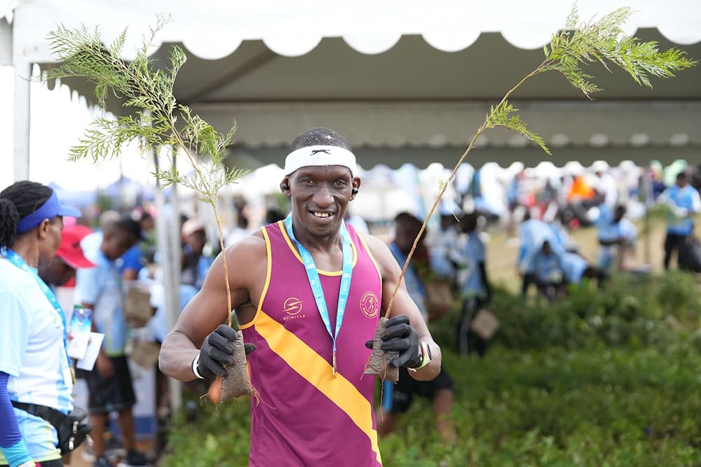 Athlete holding two small trees under a tent at an outdoor event, proudly sponsored by partners like Standard Chartered Nairobi Marathon and GPF Kenya.