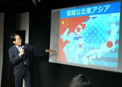 A person in a suit points to a projected map of Northeast Asia, highlighting the flags of China, North Korea, and Japan as part of a 2024 presentation on the International Day of Peace.