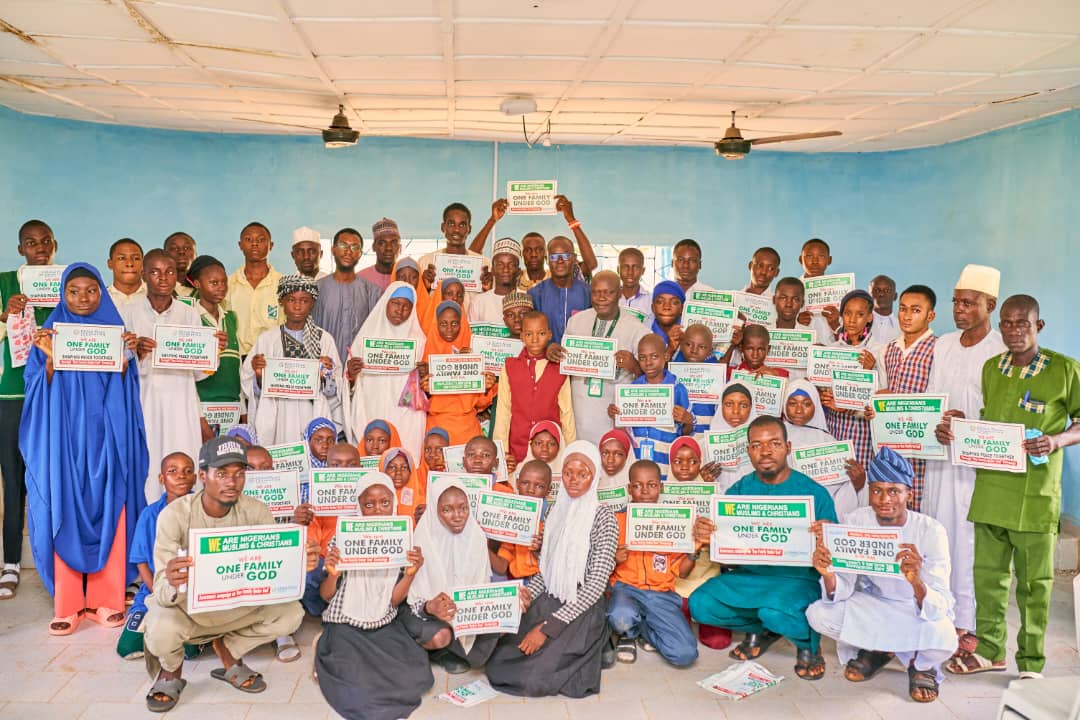 Inside a room with blue walls, a large group of people holds signs promoting unity and harmony, celebrating the International Day of Peace 2024.