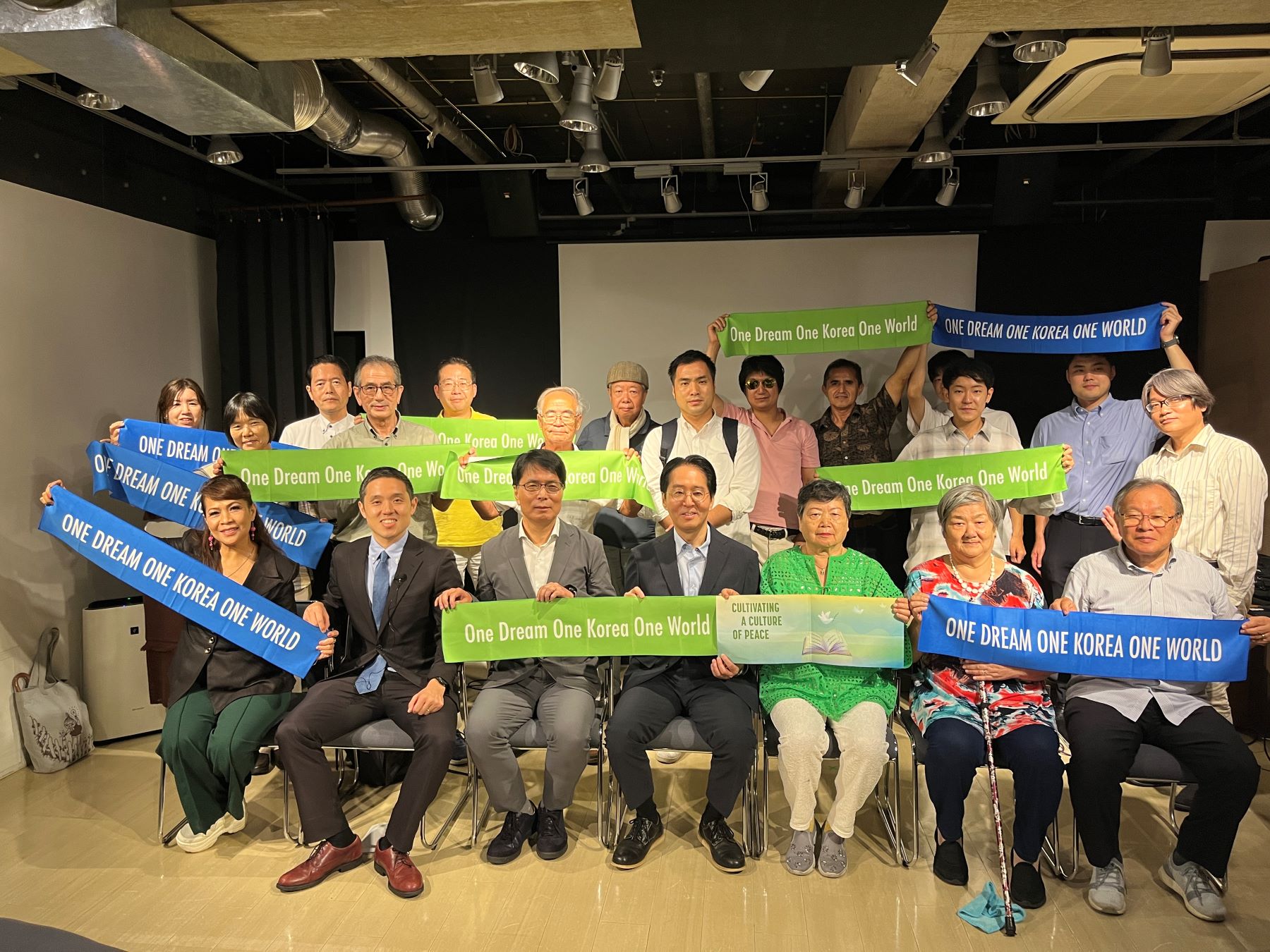 A group of people holding banners that read "One Dream One Korea One World" pose for a photo in a room, highlighting the spirit of the International Day of Peace 2024.