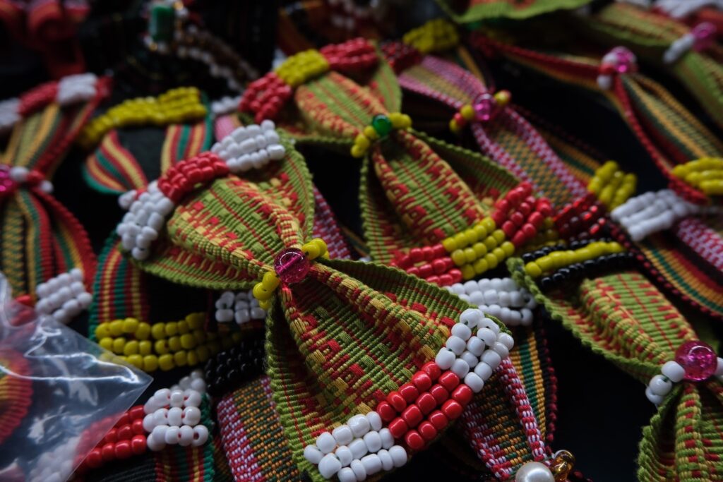 A collection of colorful beaded decorations with red, yellow, green, and white patterns from the Bead-makers Association is displayed closely together.