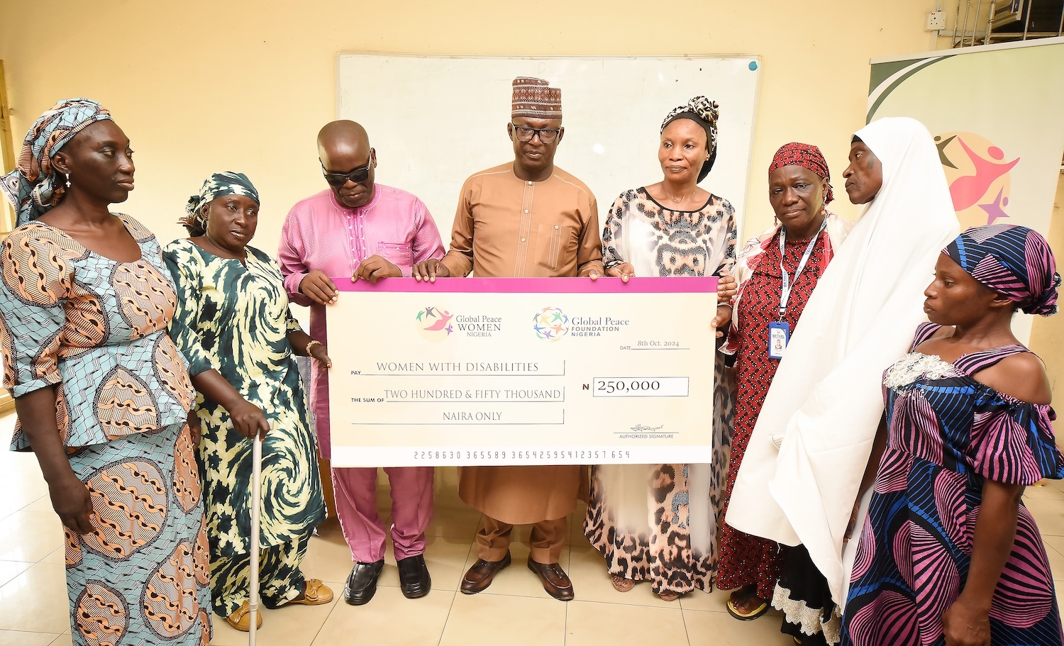 A group of people in colorful clothing hold a large check for 250,000 Naira, aimed at fostering inclusivity for women with disabilities in Kaduna State.