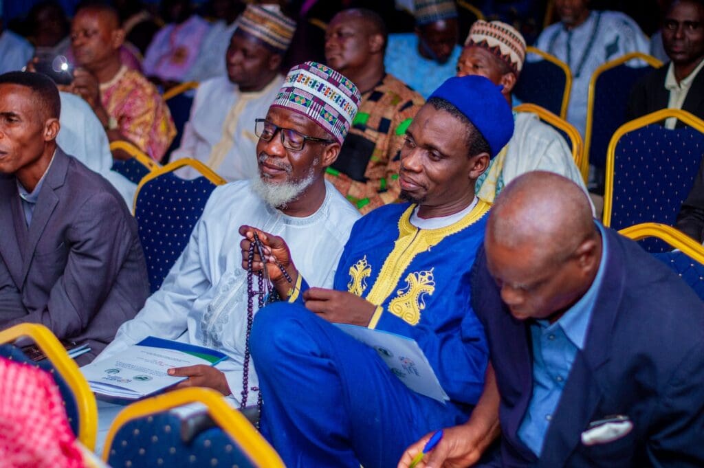 A group of men in traditional and formal attire sit in a row during the Kaduna Peace Conference, with some holding programs.