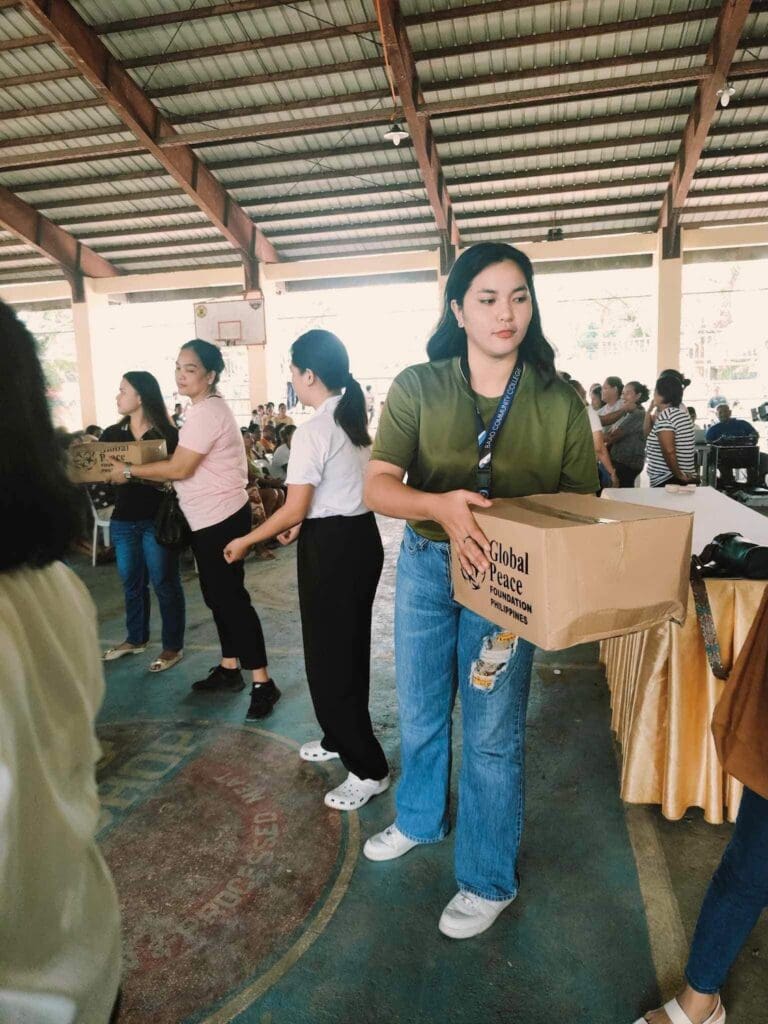 At a community event in a covered gymnasium, people distributed boxes with support from the Global Peace Foundation, bringing relief and hope to Bicol communities affected by Typhoon Kristine.