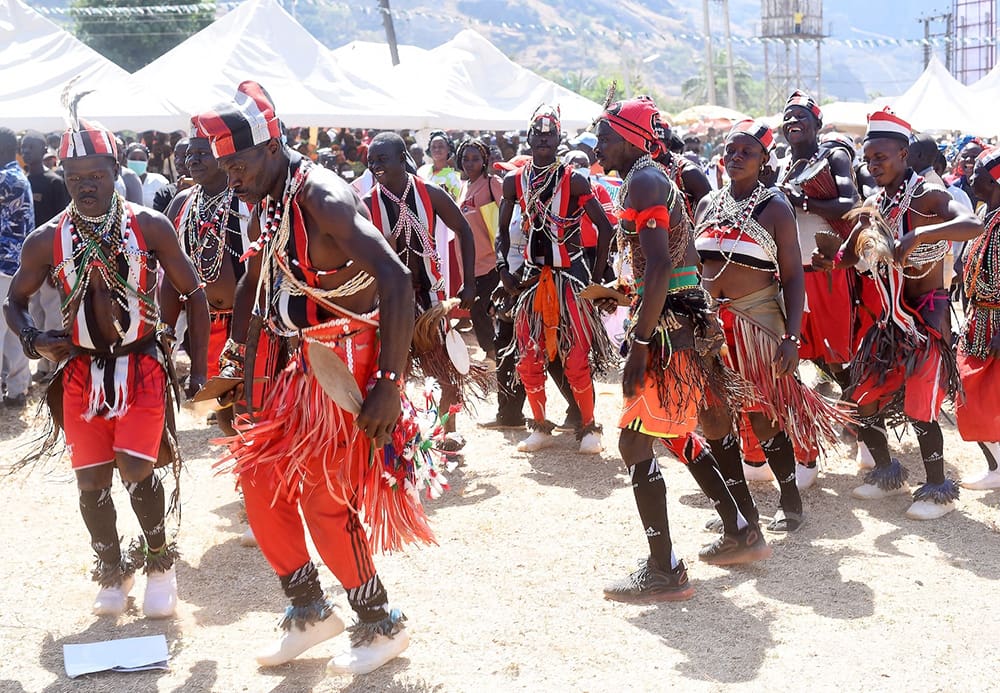 A group of people in traditional attire, featuring red and black colors, perform a cultural dance at the AFAN Festival in Kaduna State. The vibrant scene embodies unity and culture, set against an outdoor event backdrop with tents and a lively crowd.