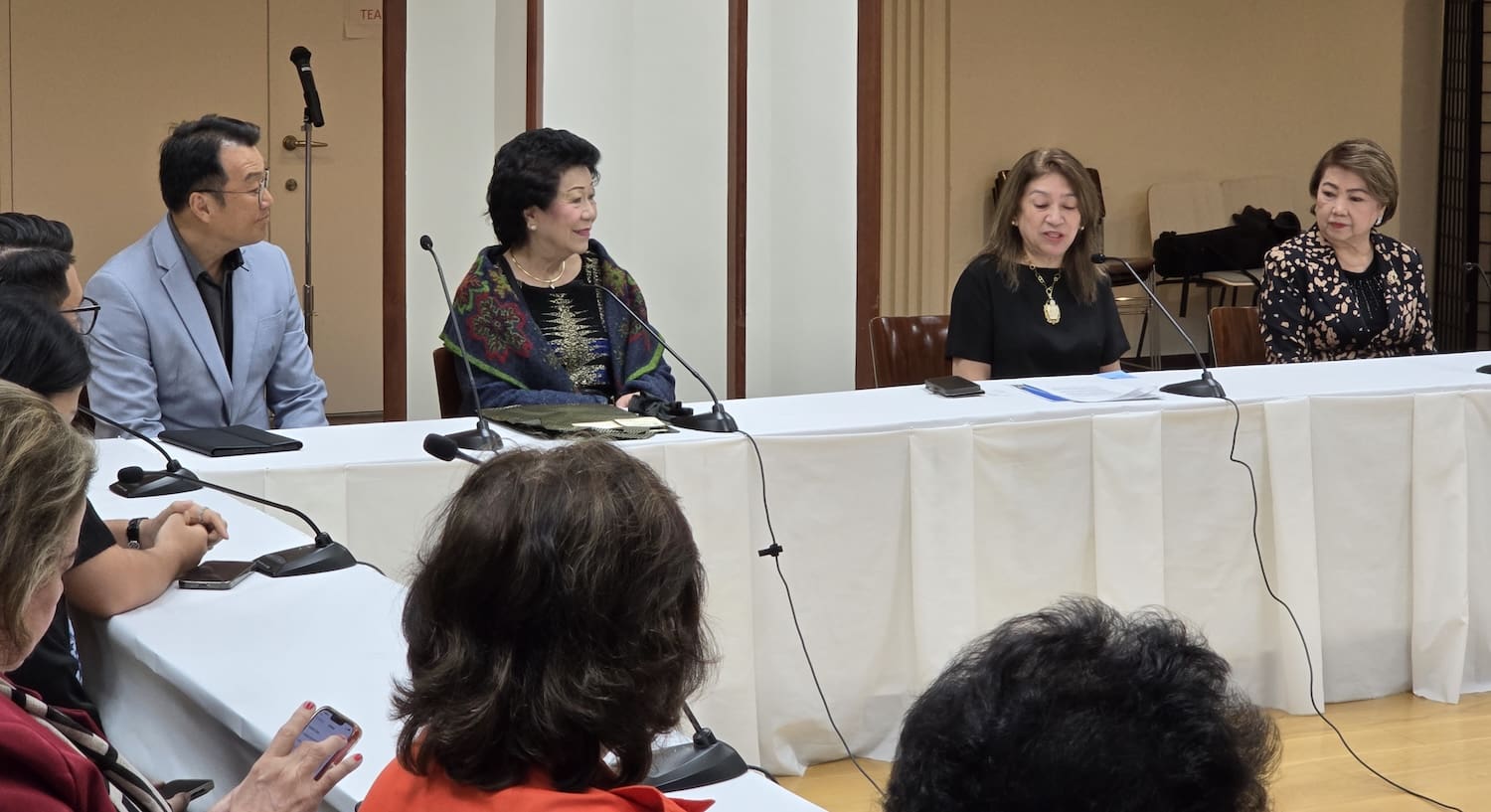 Four people are seated at a conference table with microphones, exchanging insights on Japan-Philippines collaboration to advance peacebuilding efforts. Their discussion emphasizes cross-cultural understanding and leadership development as key pillars for a harmonious future.