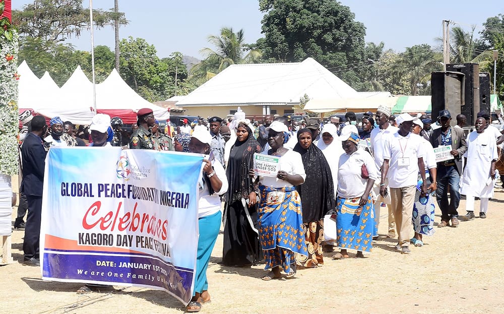 A group of people, some in traditional attire, walk in a parade holding a banner that reads