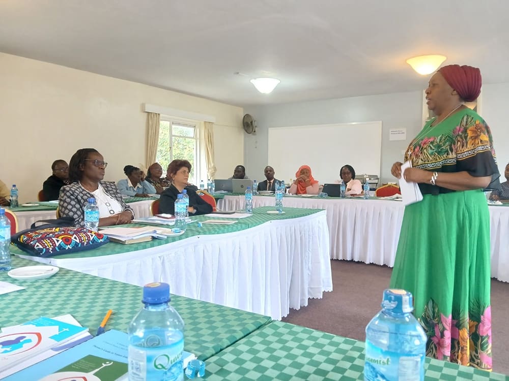 In a conference room adorned with green checkered cloths, a speaker eloquently addresses the seated group, emphasizing the importance of strengthening families through values education. Bottled water is neatly arranged on tables as attendees engage in this dialogue promoting an African renaissance.