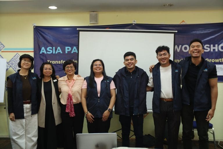 Seven people standing in front of a banner and screen, smiling at the camera.