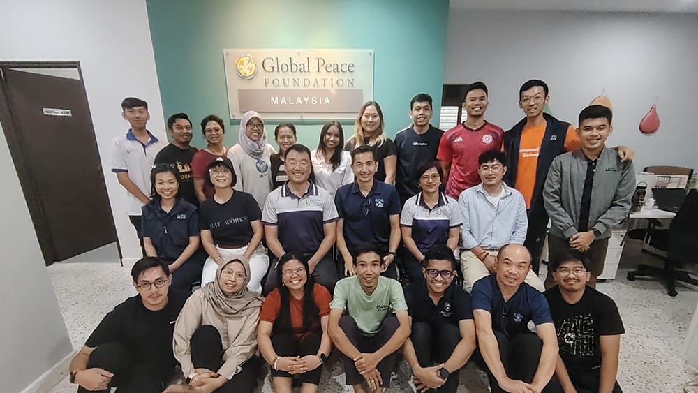 A group of 25 people of diverse backgrounds posing in front of a sign that reads