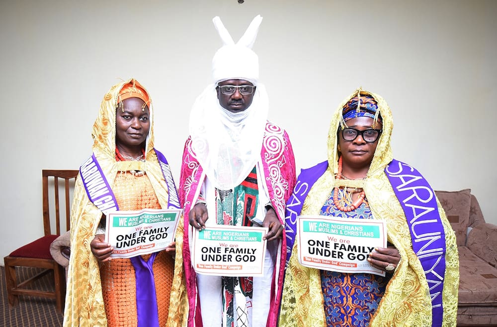 Three people stand holding signs that read