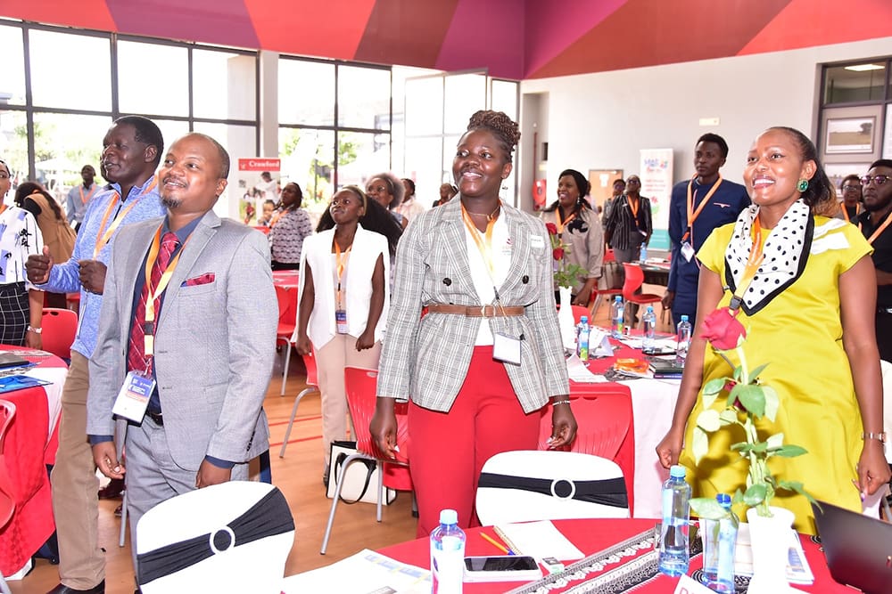A group of people standing in a brightly lit room with conference badges, smiling and looking forward.