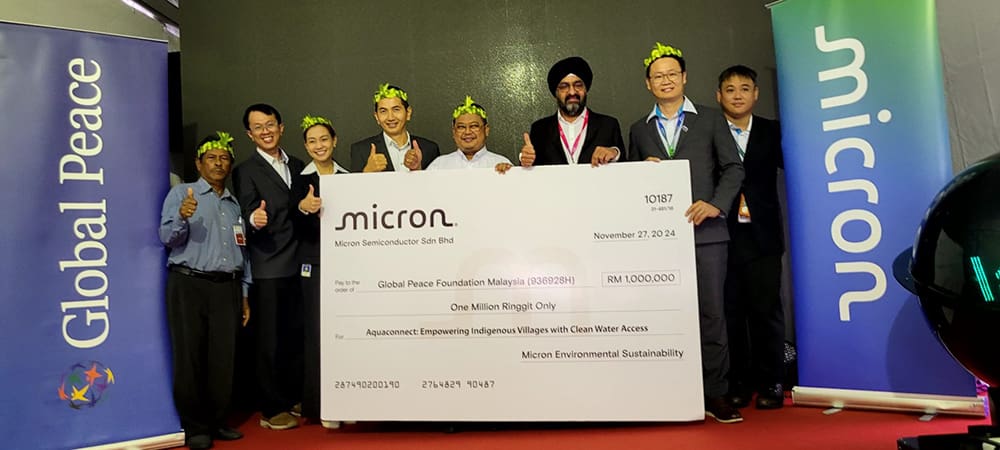 A group of people holds a large ceremonial check from Micron for One Million Ringgit, dated November 27, 2014. Banners for Global Peace and Micron are in the background, highlighting their commitment to clean water projects benefiting the Orang Asli community.