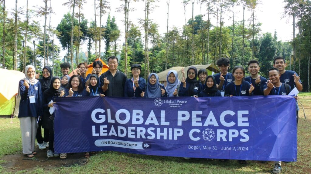 A group of young adults and a leader, representing Global Peace Leadership Corps Indonesia, stand outdoors behind a banner that reads