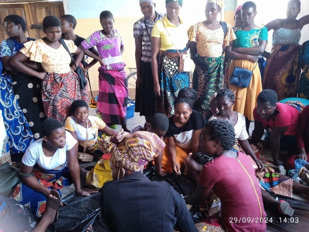 A group of women and girls, some seated and some standing, gather indoors in colorful clothing, engaging in a discussion or activity—highlighting strong family ties. The date and time are shown on the photo. Sunshine Family Volunteers support this event in Malawi.