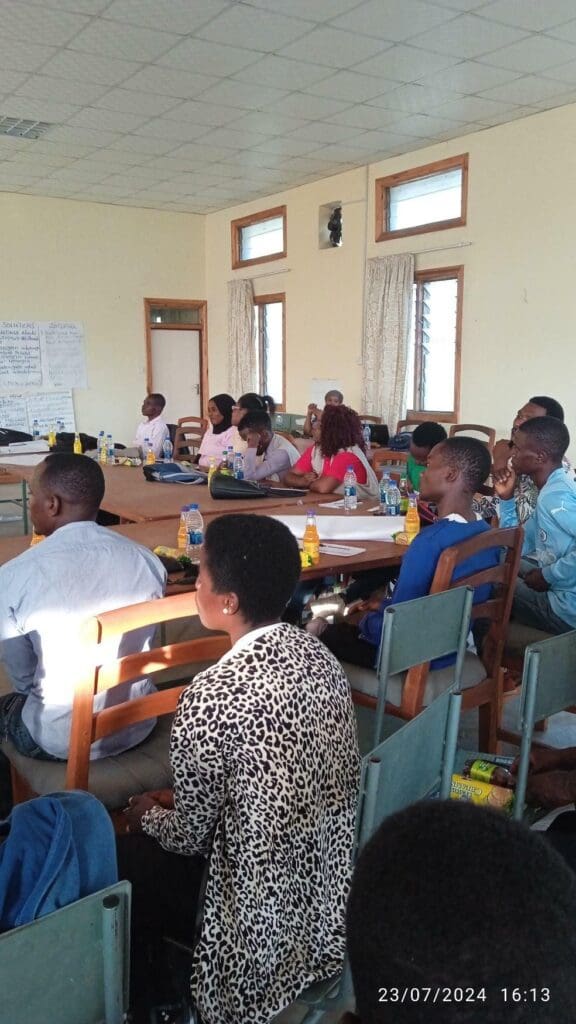 A group of people seated around tables in a meeting room, listening attentively; bottled drinks and papers are on the tables—members of Sunshine Family Volunteers discuss ways to Rebuild Family Ties in Malawi.