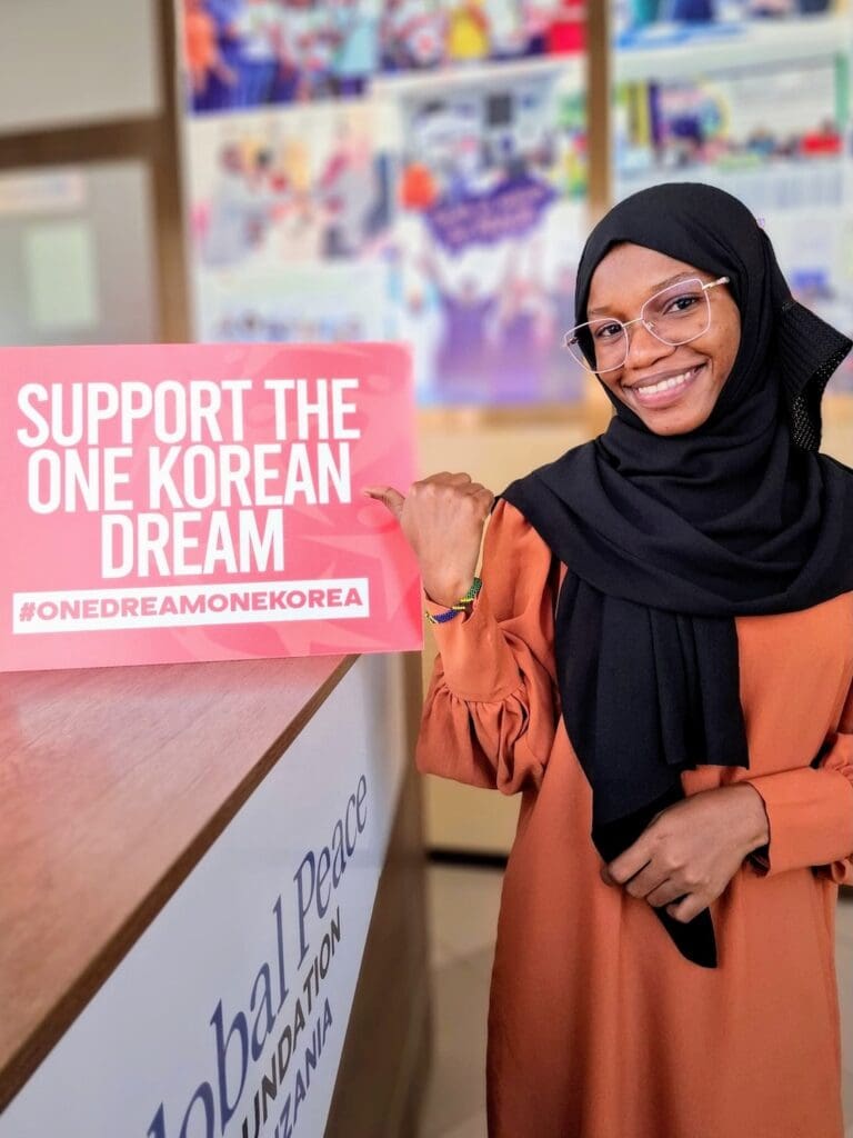 A woman in a hijab smiles and holds a sign that reads 